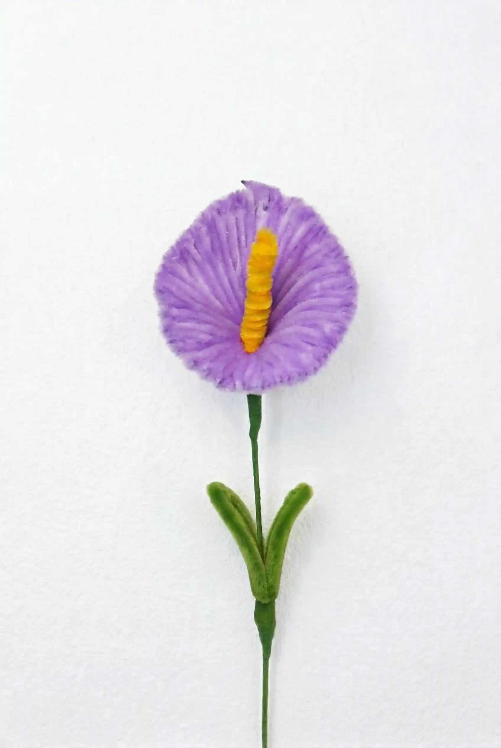 Top-down view of a finished artisan-made purple Anthurium with a yellow spadix, showing the heart-shaped spathe.