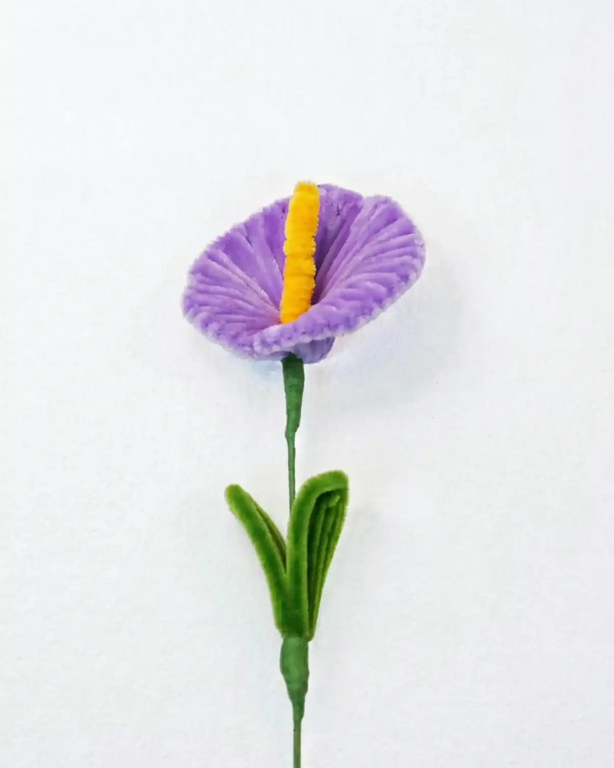 Top-down view of a finished artisan-made purple Anthurium with a yellow spadix, showing the heart-shaped spathe.