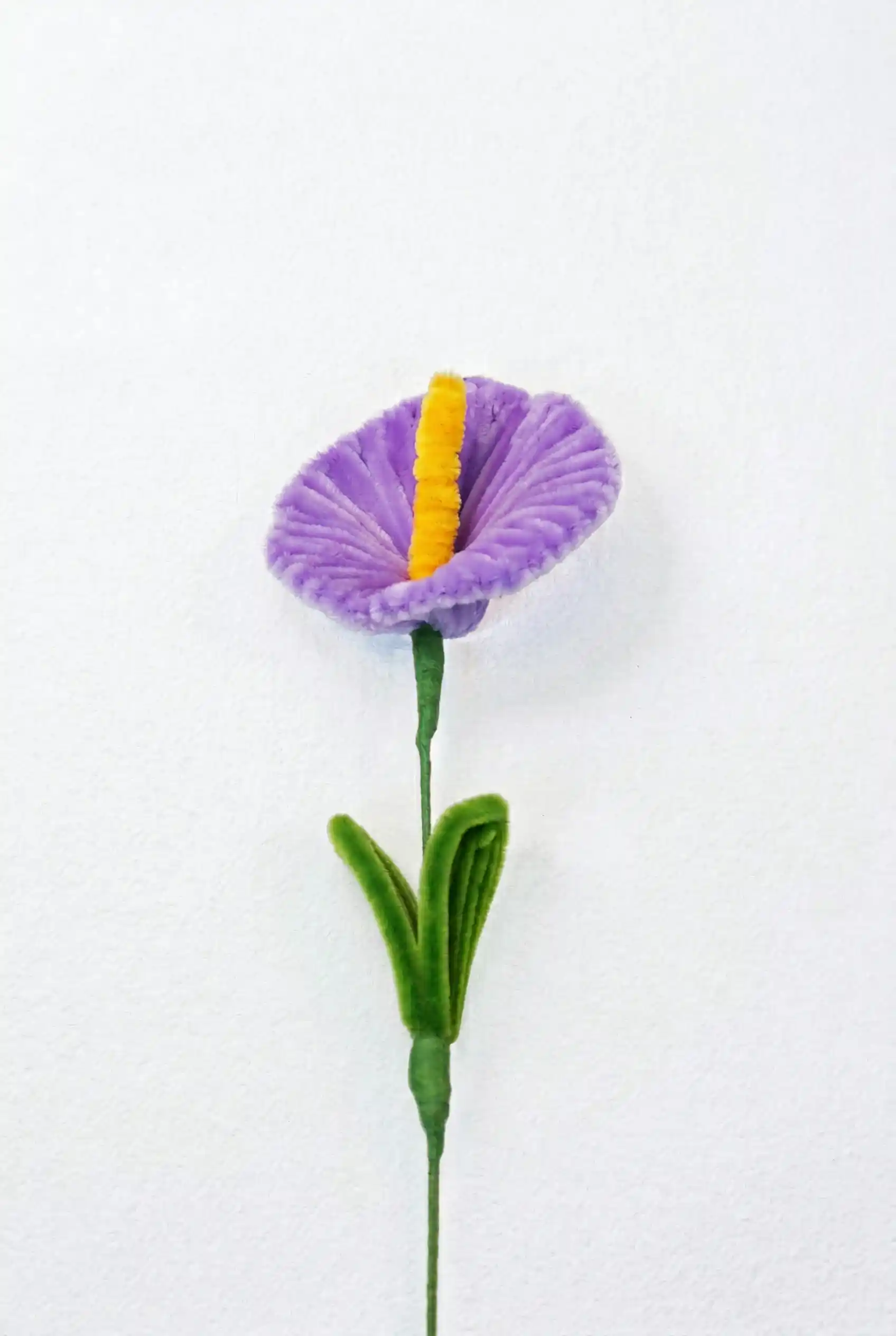 Top-down view of a finished artisan-made purple Anthurium with a yellow spadix, showing the heart-shaped spathe.