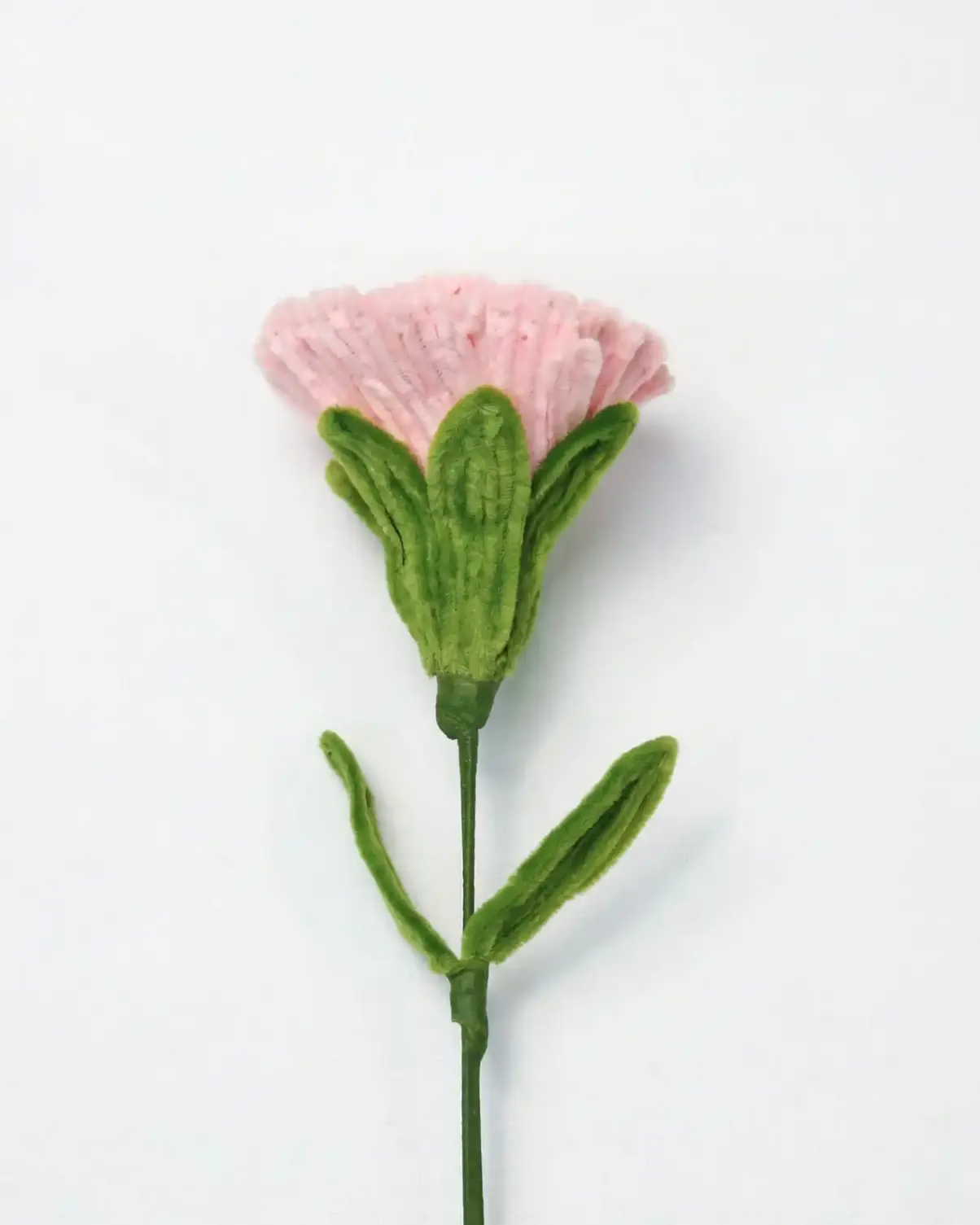Side view of a finished artisan-made pink carnation, highlighting the green calyx and velvet texture.