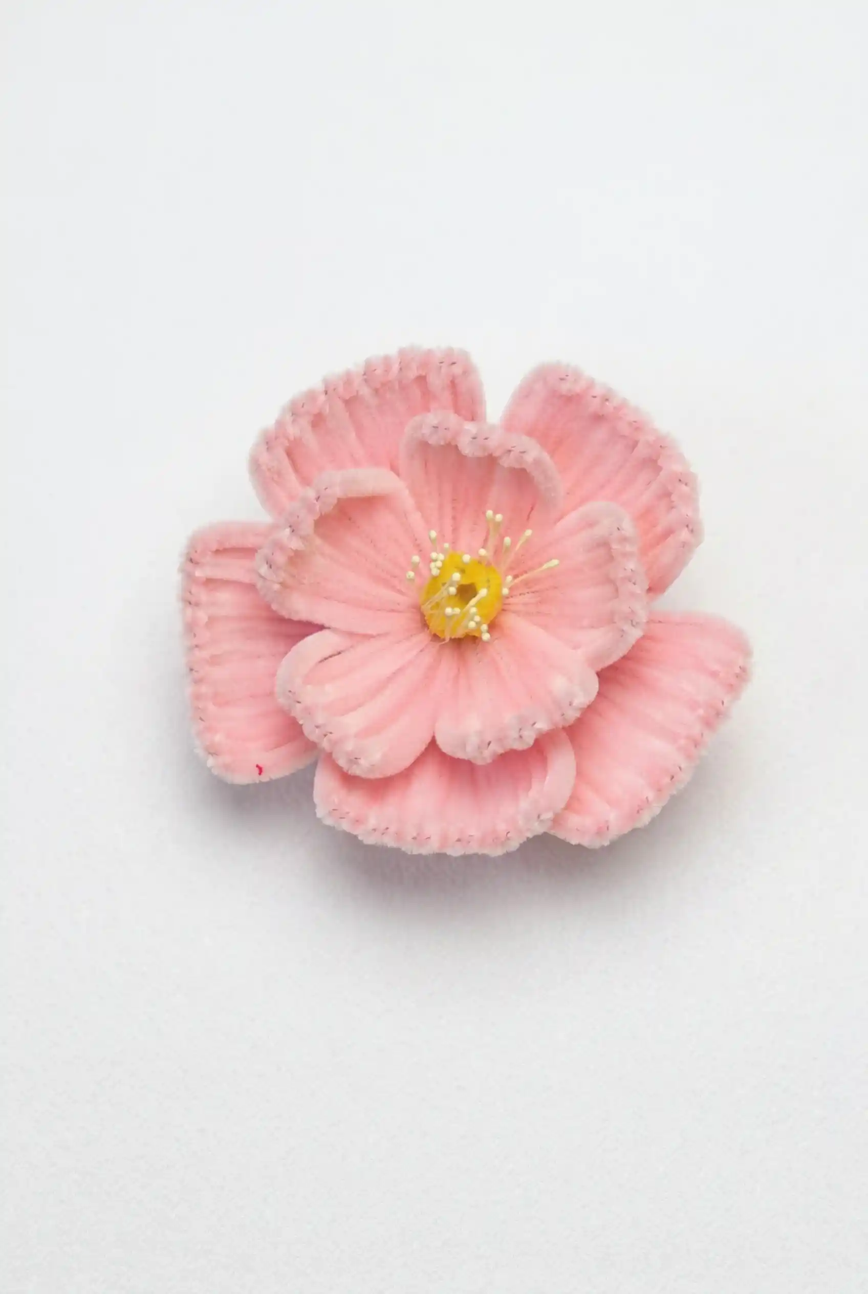 Top-down view of a finished handmade pink Peony soft sculpture by Glint Garden, showing dense velvet petals and a yellow center.