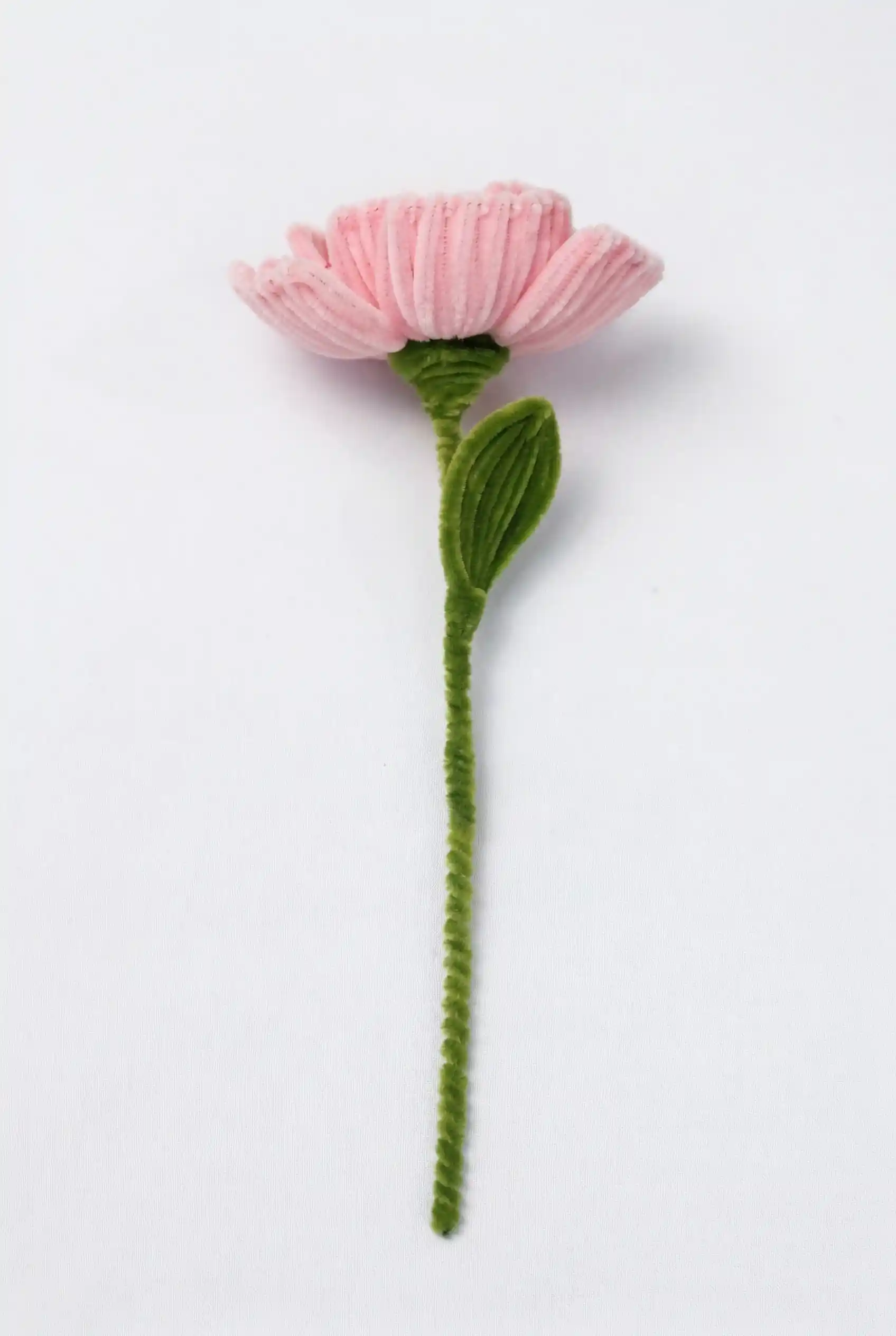 Side profile of a finished artisan-made pink Peony with a single green leaf on a long stem, ready for home decor.