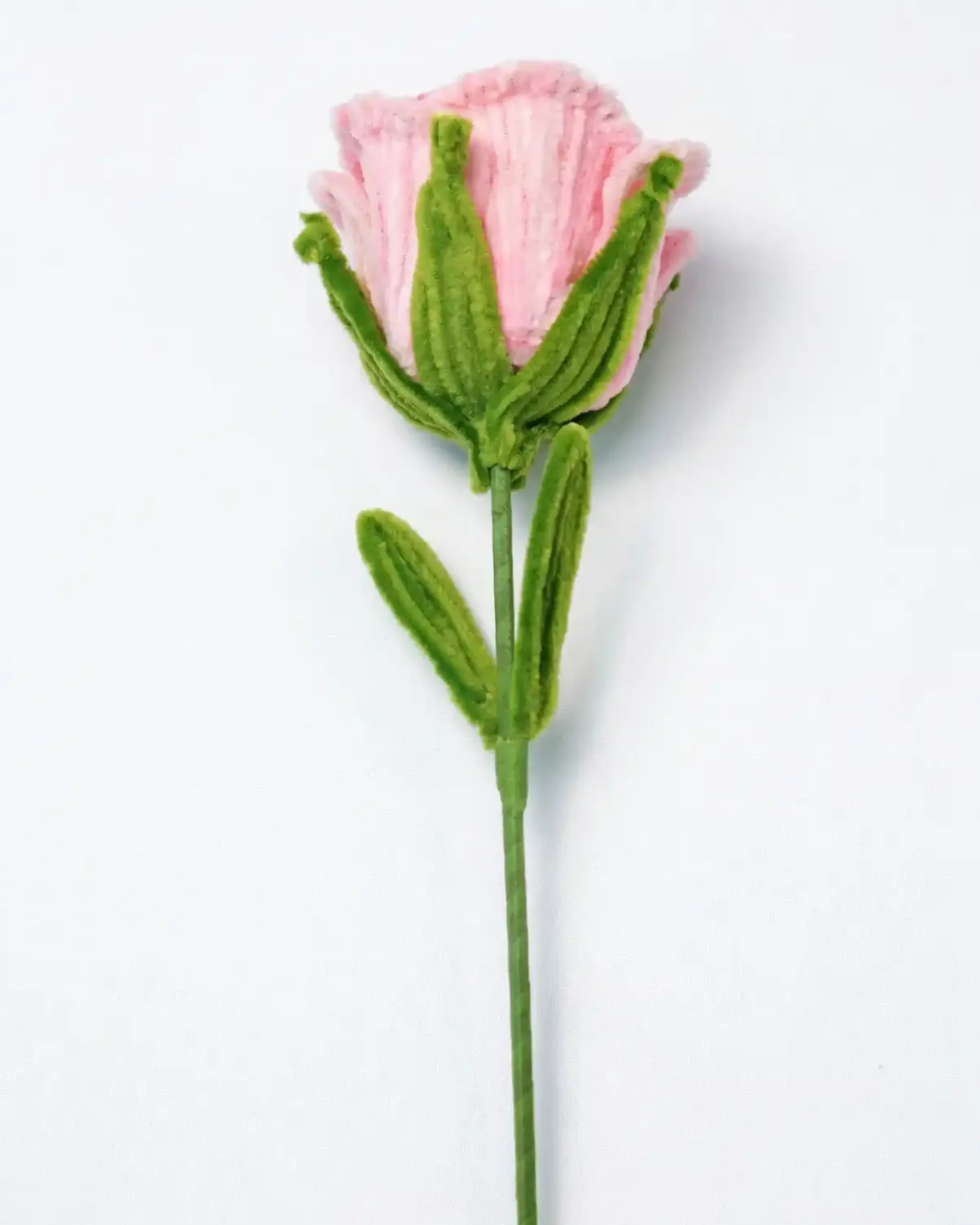 Side profile of a finished artisan-made ruffled pink rose with green leaves on a long stem.