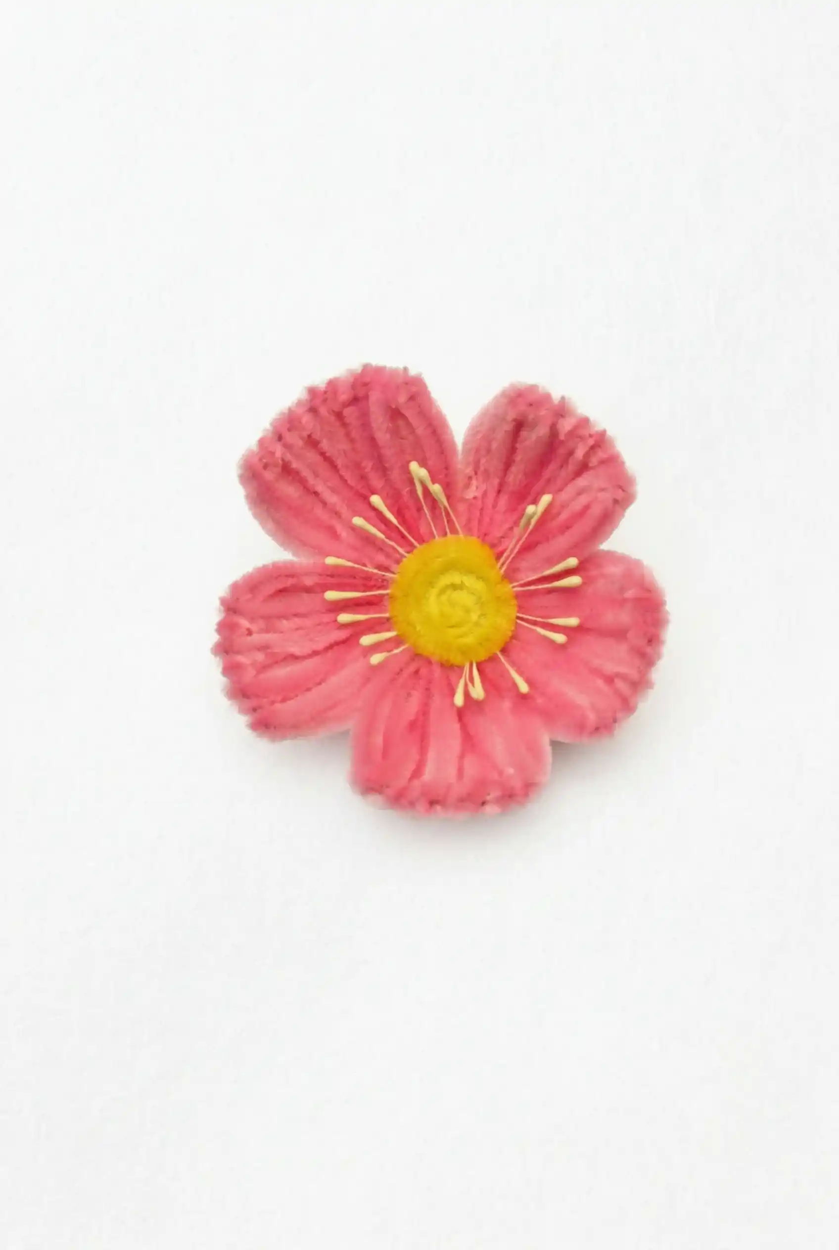 Top-down view of a finished handmade pink Poppy soft sculpture by Glint Garden, featuring a sunny yellow center.
