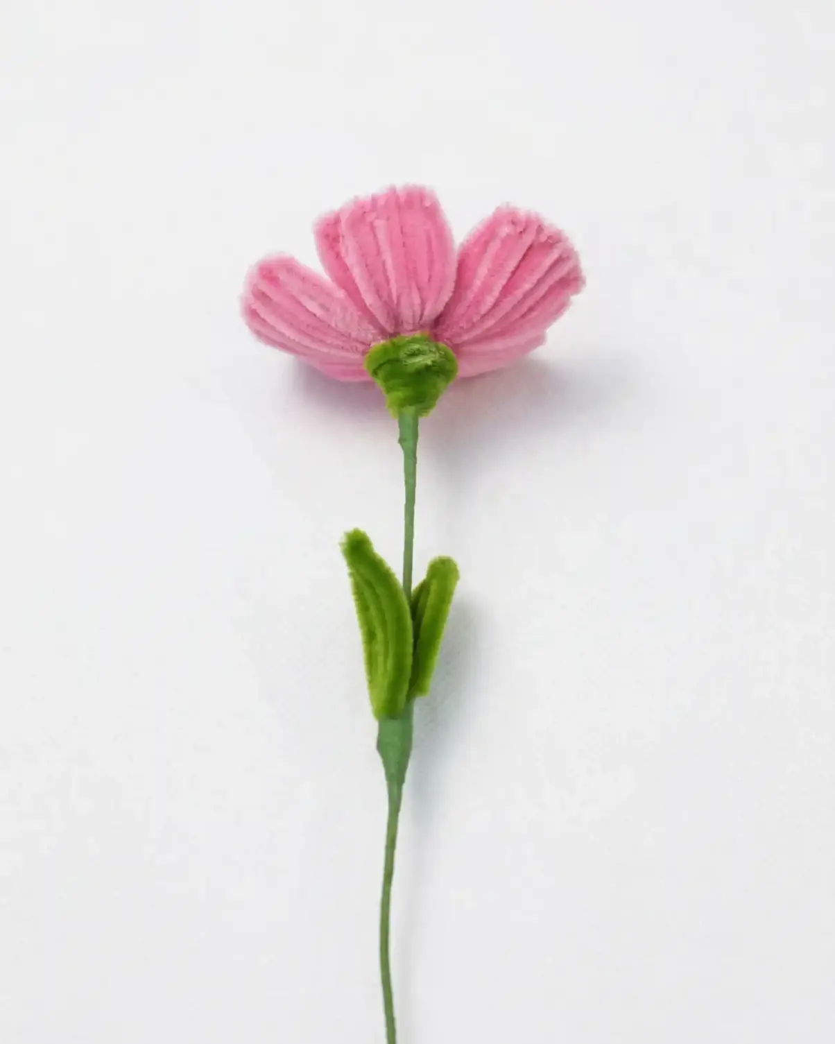 Side view of a finished artisan-made pink poppy flower with green leaves on a long stem, a whimsical home decor piece.