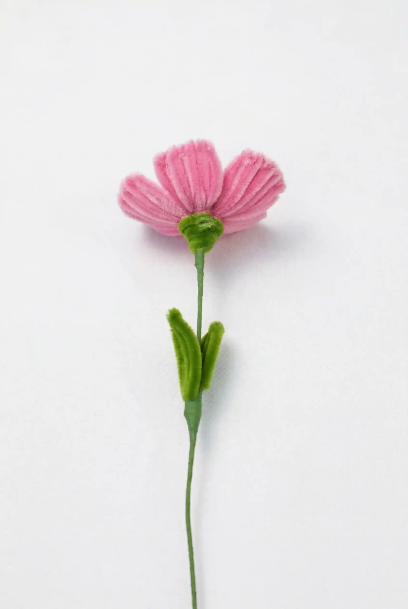 Side view of a finished artisan-made pink poppy flower with green leaves on a long stem, a whimsical home decor piece.