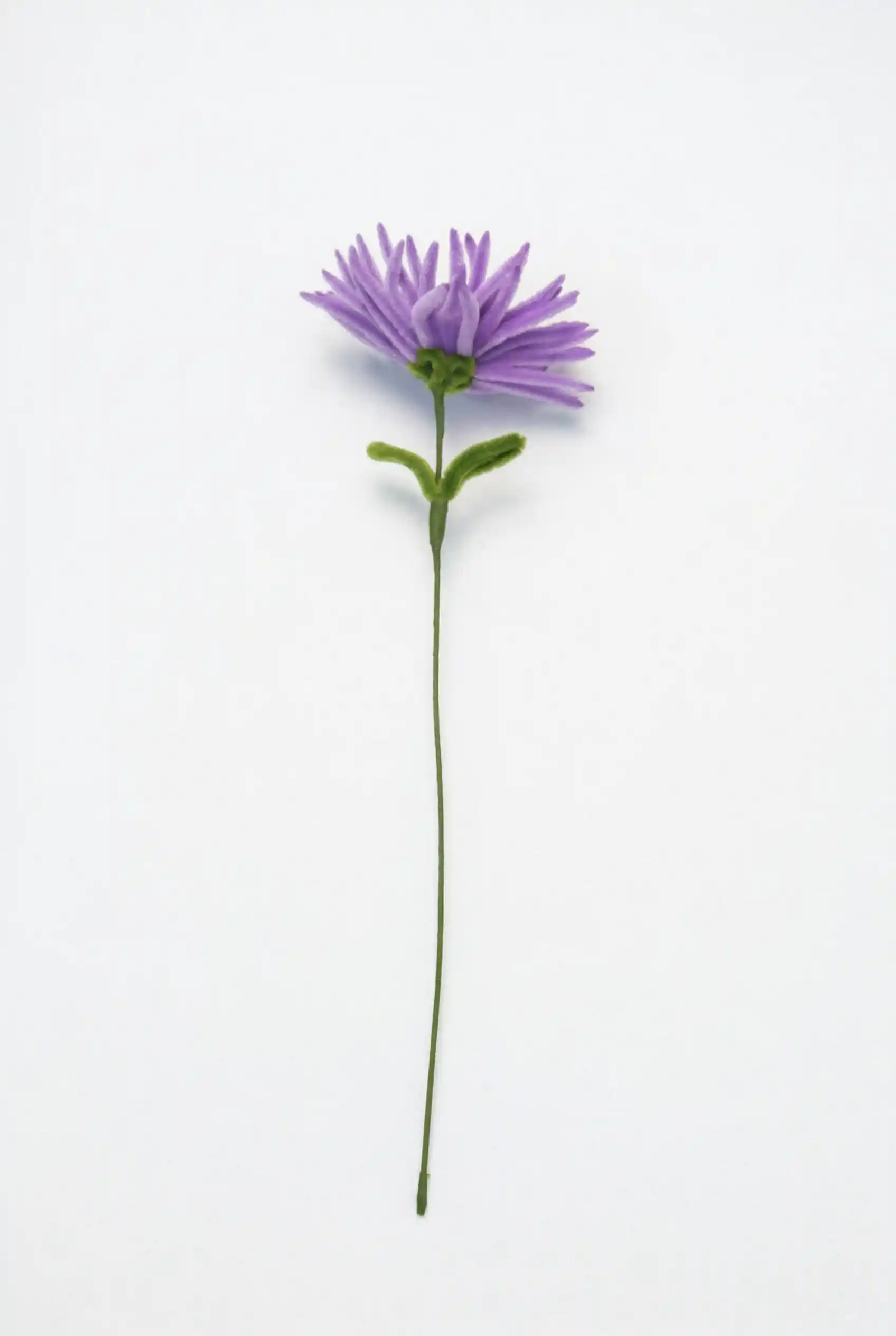 Side view of a finished artisan-made purple spider mum, showing the sculptural silhouette and green leaves.