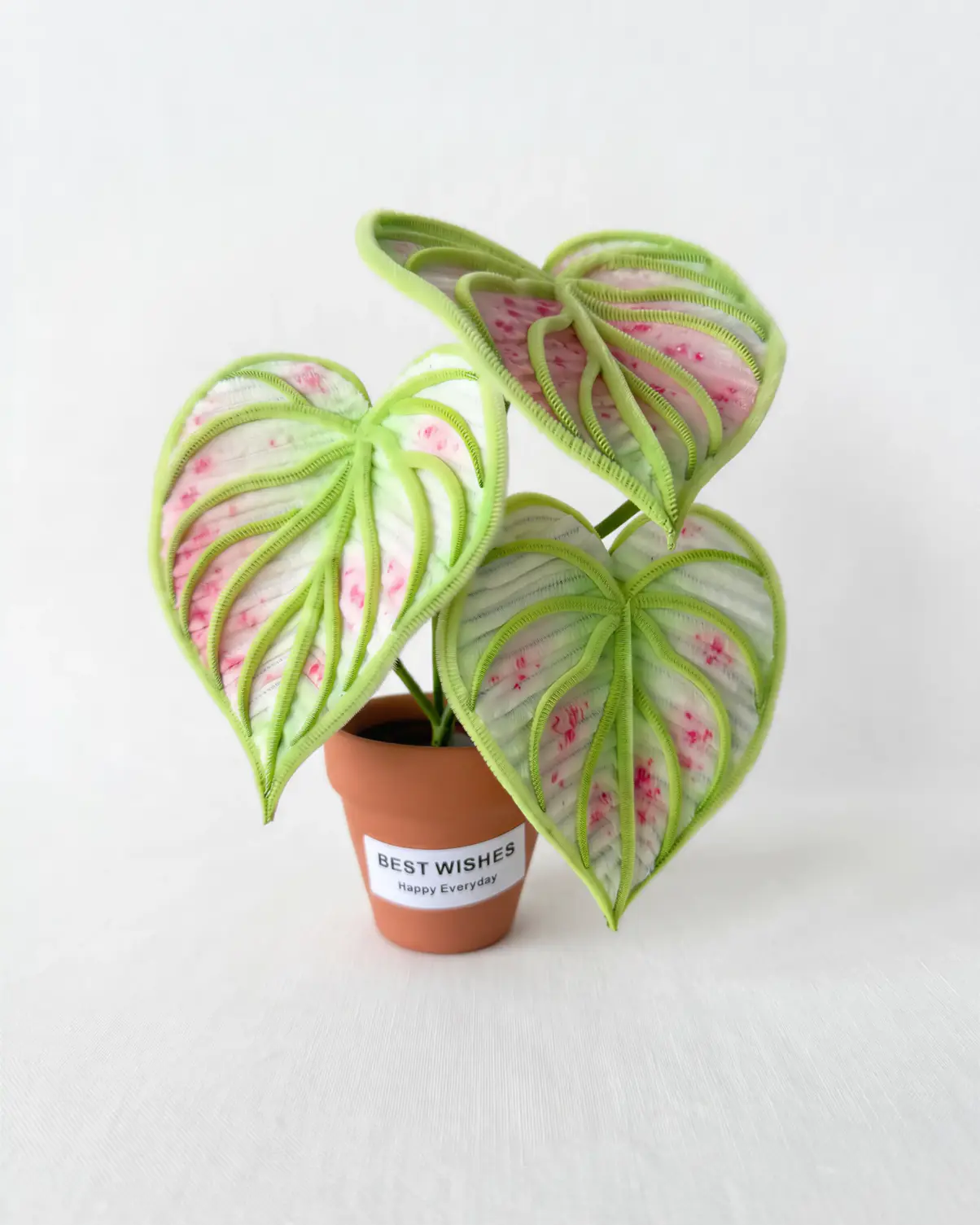 A realistic handmade pink and green variegated Caladium (Angel Wings) plant made from chenille stems in a terracotta pot.