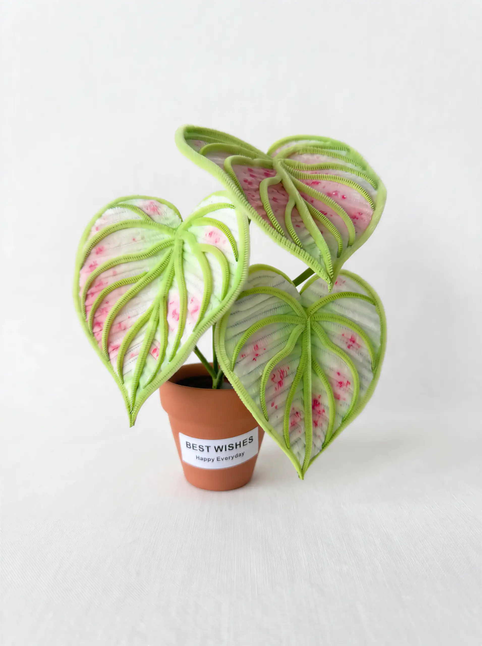 A realistic handmade pink and green variegated Caladium (Angel Wings) plant made from chenille stems in a terracotta pot.