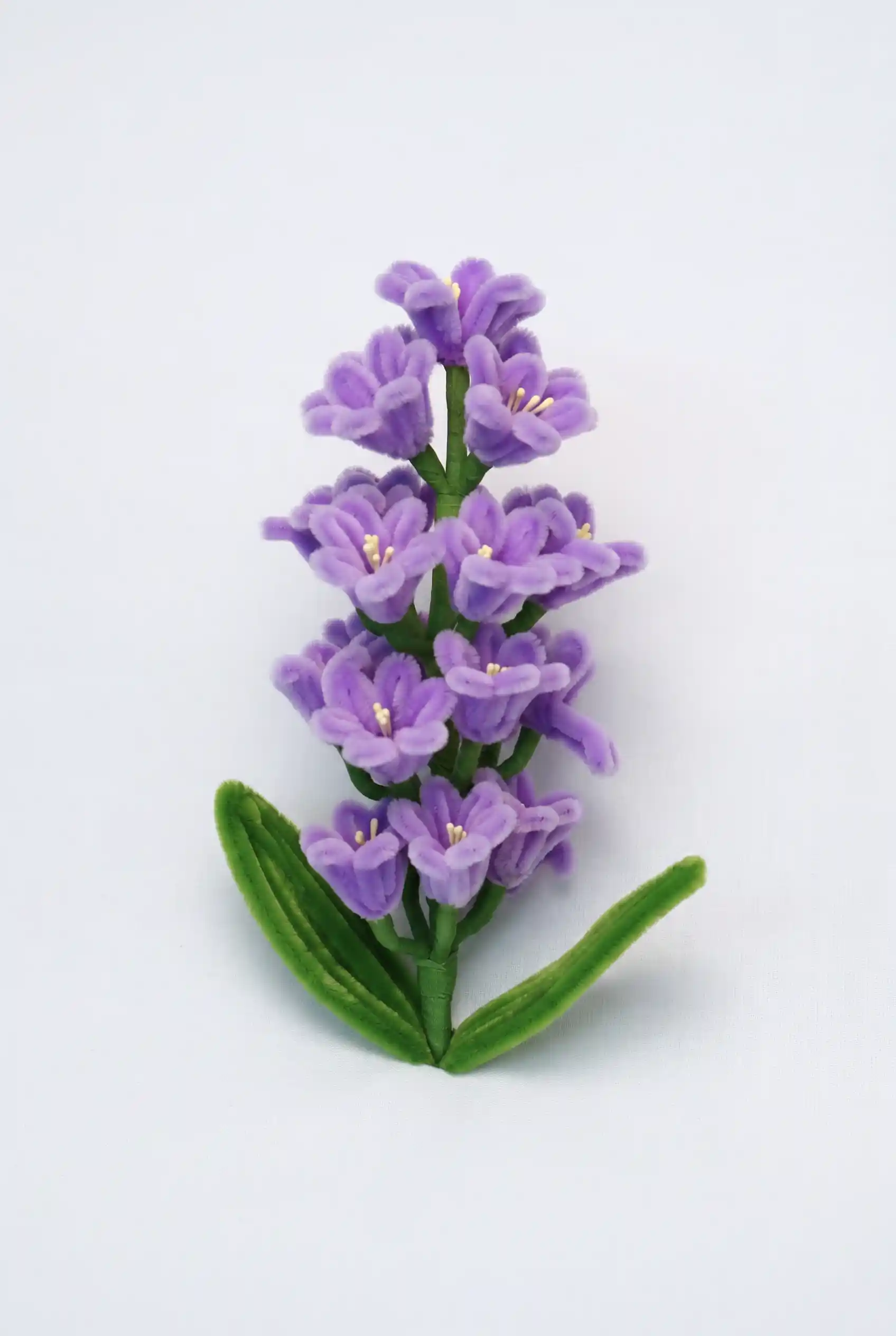 Full stem view of a finished handmade purple hyacinth soft sculpture with bell-shaped florets and green leaves.