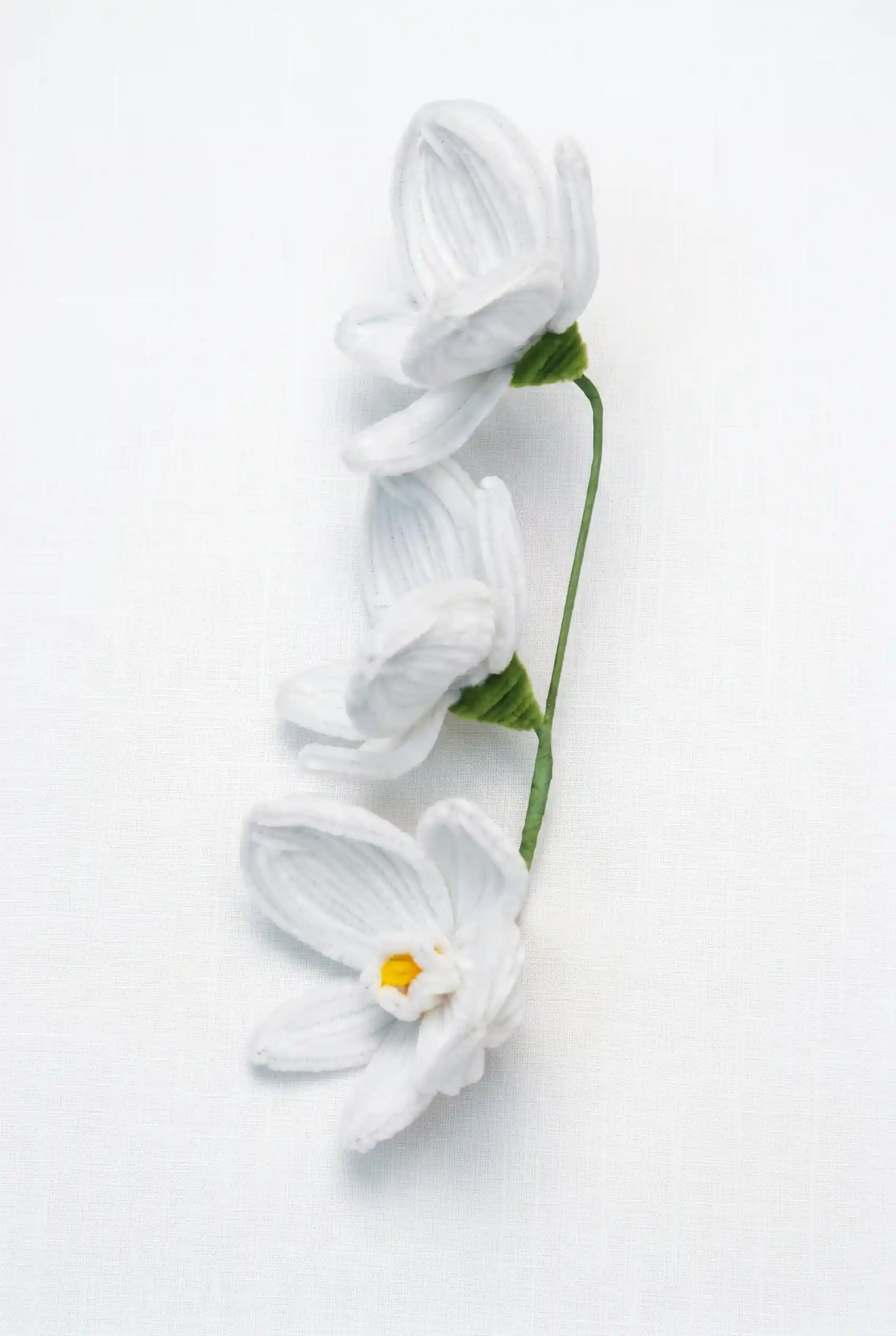 Side profile of a finished artisan-made white orchid stem, showing the delicate curvature and velvet texture.